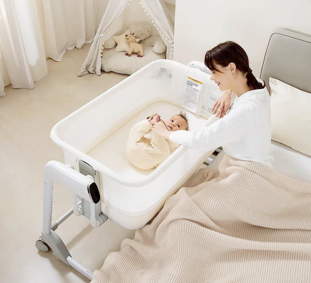 Rever Bebe Smart Dream electric bassinet — beside a bed with a parent and baby