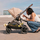 Almond Beige e-Gazelle S outdoors with its seat reclined, a parent alongside and shopping in the basket below.