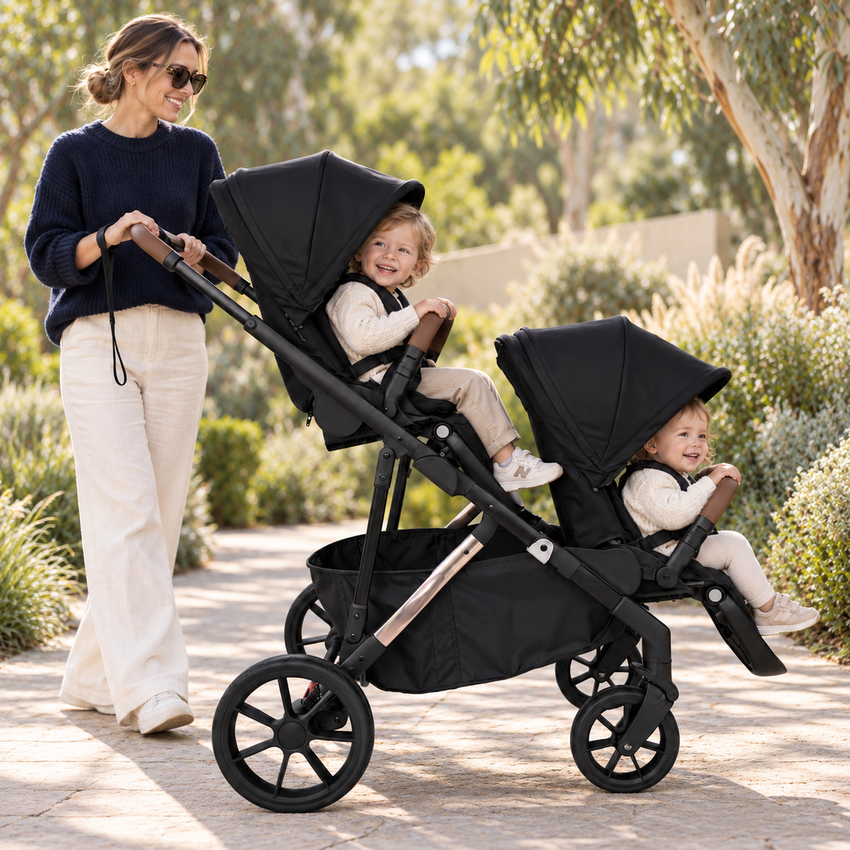 Black Rever Bebe VEVO double pram with two seated children on a garden path